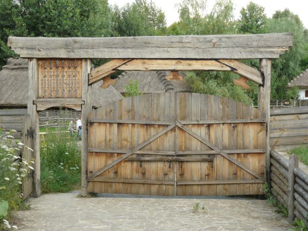 Large wooden gates in light grey tone with arching top and crossbar at center.